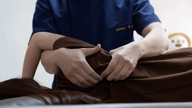 엎드린 환자의 어깨를 손으로 치료하는 모습